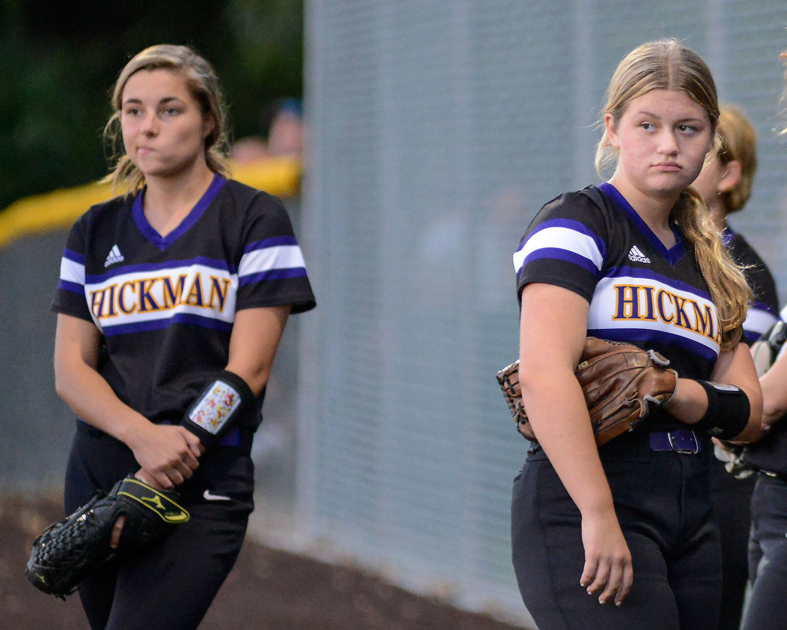 Hickman players Emma Henley, left, and Shelby Bryan look onto the field after Hickman loses to Rock Bridge in softball
